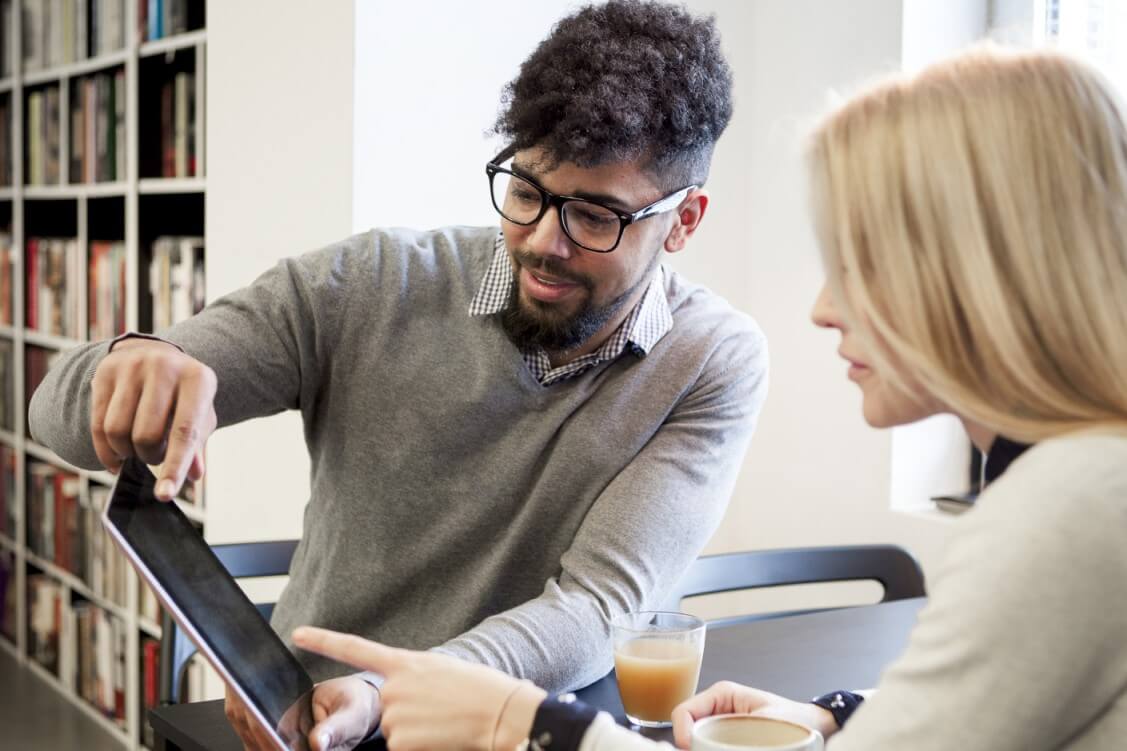 Two college students sit in the library and work on a tablet